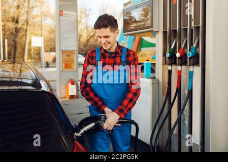 Lavoratore maschile in auto a combustibili uniformi su stazione di benzina, rifornimento di carburante. Rifornimento di benzina, rifornimento di benzina o diesel Foto Stock