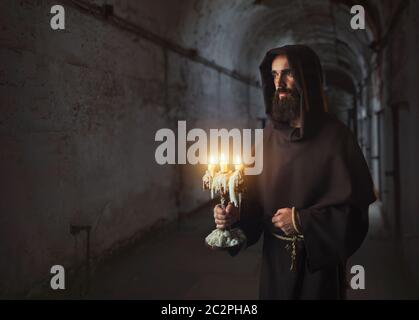 Monaco medioevale in accappatoio detiene un candelabro in mani nel tempio, segreto rituale. Misterioso frate con candele. Mistero e spiritualità Foto Stock