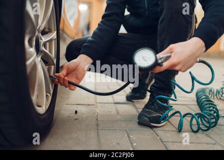 La persona di sesso maschile controlla la pressione degli pneumatici, la manutenzione degli pneumatici. Servizio di riparazione di veicoli o attività, l'uomo gonfia le ruote su automobile all'aperto Foto Stock