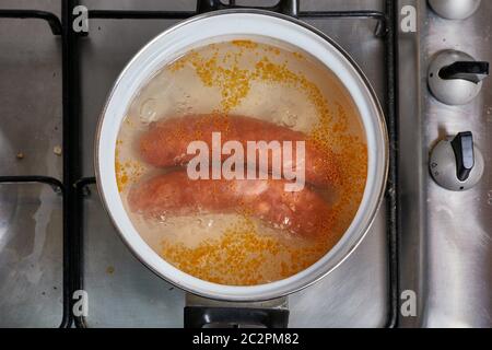 Preparazione di una coppia di salsicce sul fornello a gas Foto Stock