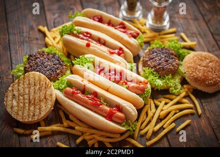 Un fast food assortimento. Hamburger e hot dogs collocato su rusty tavolo in legno Foto Stock