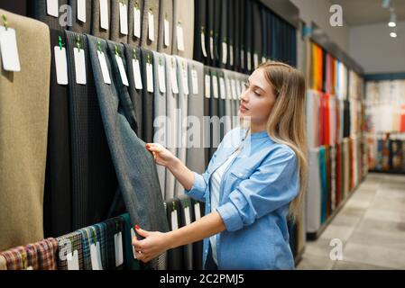 Il venditore misura il tessuto nel deposito tessile. Ripiano con panno per cucire su sfondo, scelta di modelli di abbigliamento in negozio Foto Stock