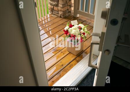 Un bouquet di fiori bianchi rossi in una scatola di cartone su un portico di porta di una casa. Sorpresa consegna senza contatto di fiori. Foto Stock