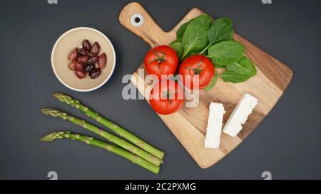 Una selezione di prodotti freschi per preparare un'insalata greca con formaggio feta, pomodori, spinaci, asparagi e olive Kalamata Foto Stock