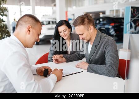 Venditore e un paio di rendere la vendita di una nuova auto nello showroom. Maschio e femmina i clienti guarda il veicolo in concessionaria, automobile vendita auto pur Foto Stock