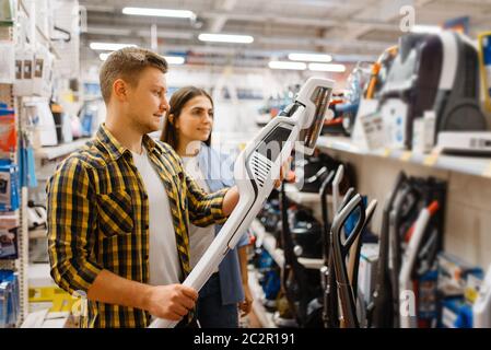 Giovane coppia che sceglie l'aspirapolvere nel negozio di elettronica. Uomo e donna che acquistano elettrodomestici sul mercato Foto Stock
