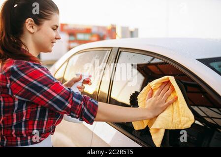 Carino donna pulisce il vetro anteriore della vettura con spugna e spray, autolavaggi. Lady on self-service di lavaggio di automobile. Esterno la pulizia del veicolo ad estate d Foto Stock