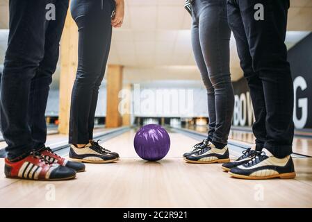 Bowling team, dei piedi dei giocatori in casa le scarpe e la sfera sulla corsia. Gli amici di giocare la partita in club, svago attivo Foto Stock