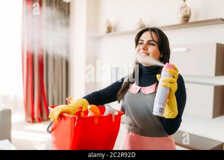 Sorridente cameriera in uniforme e guanti di gomma spray rinfrescante per l'aria nella camera di albergo. Il servizio di pulizie professionali attrezzature, charwoman Foto Stock