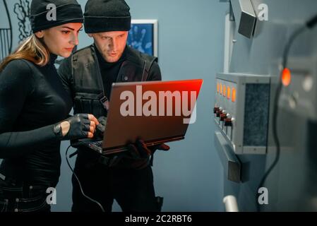 Rapina bancaria, due ladri con il computer portatile che cercano di aprire la porta del vault. Professione criminale, concetto di furto Foto Stock
