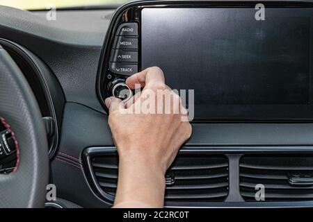 Primo piano della mano della donna, pulsante di accensione sulla radio dell'auto per ascoltare la musica. Interni moderni. Foto Stock