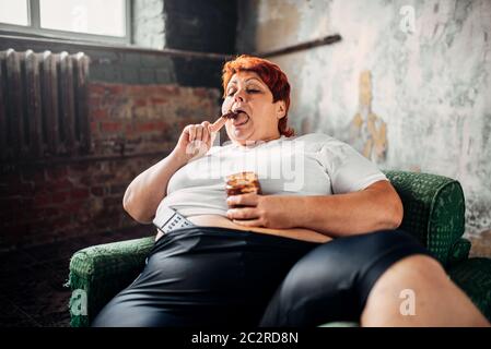 Il sovrappeso donna si siede su una sedia e mangia caramelle. Uno stile di vita poco salutare, obesità Foto Stock