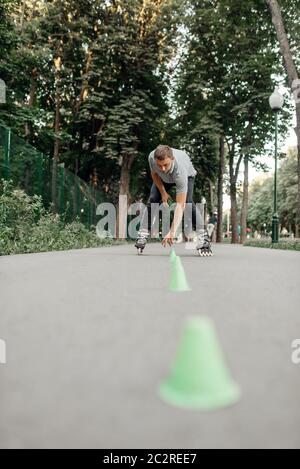 Pattinaggio a rotelle, pattinatore maschile mette i coni nel parco. Pattinaggio urbano, sport estremi attivi all'aperto, tempo libero per i giovani, pattinaggio a rotelle Foto Stock