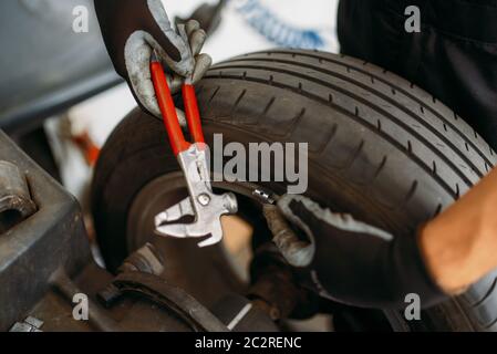 Ruota di equilibratura meccanica automatica su macchina speciale, servizio pneumatici. Uomo ripara pneumatico auto in garage, ispezione professionale auto in officina Foto Stock