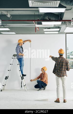 Immagine verticale lunga di operai edili professionisti che effettuano misurazioni della lunghezza utilizzando la riga del nastro e lo spazio di copia Foto Stock