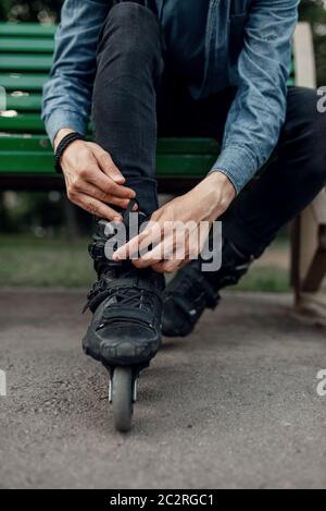 Pattinaggio a rotelle, pattinatore maschile mette su pattini nel parco. Pattinaggio urbano, sport estremi attivi all'aperto, tempo libero per i giovani, pattinaggio a rotelle Foto Stock