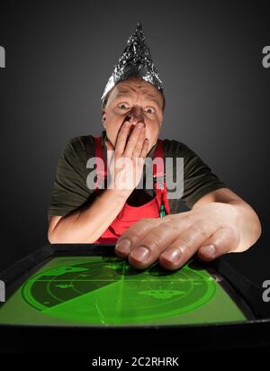 Spaventata uomo che indossa un cappello di lamina e guardando vecchi monitor del radar con ufo Foto Stock