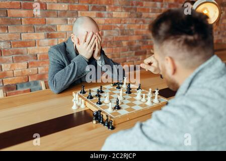 Maschio di giocatori di scacchi gioca a bordo, vince il bianco, mate. Due chessplayers iniziare il torneo intellettuale all'interno. La scacchiera sul tavolo di legno Foto Stock