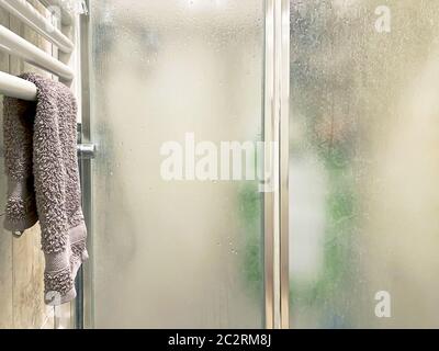 asciugamano di colore viola disposto su un radiatore bianco vicino al box doccia con porte in vetro smerigliato Foto Stock