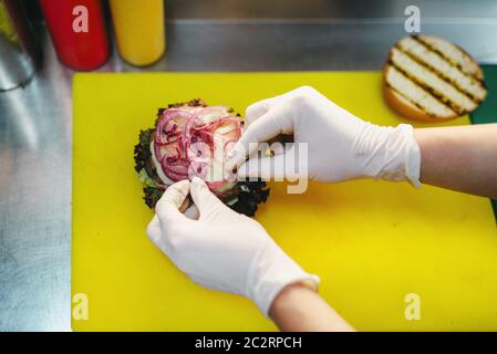 Voce maschile cuoco prepara insalate fresche di Burger. Hamburger processo di preparazione, un fast food per la cottura Foto Stock