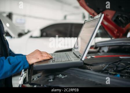 Ingegnere calcolatore rende la diagnostica della vettura in auto service. Cablaggio del veicolo ispezione Foto Stock