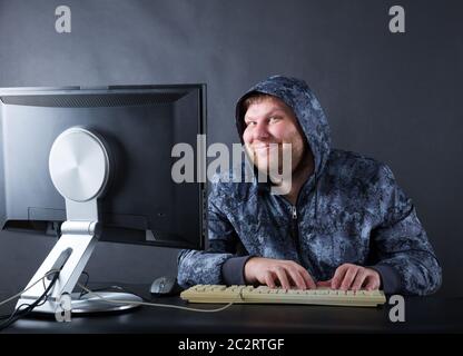 Fat uomo sorridente seduto alla scrivania guardando lo schermo del computer Foto Stock