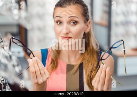 Donna che sceglie tra due modelli di occhiali a optometristo che li tiene davanti al suo viso Foto Stock