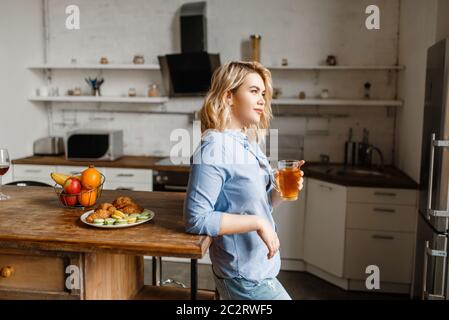 Giovane donna che si serve la colazione con croissant e biscotti. La donna mangia dessert in cucina, buon mattino, felice stile di vita Foto Stock