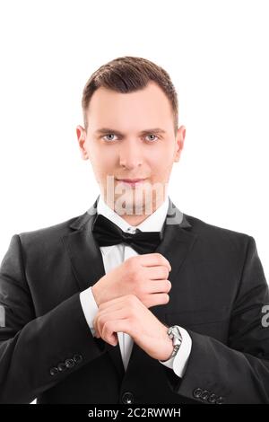 Primo piano ritratto di un uomo sicuro, stupefacente, trendy, attraente, sognante, perfetto in tuta nera con cravatta ad arco, che regola i gemelli sui suoi bianchi Foto Stock