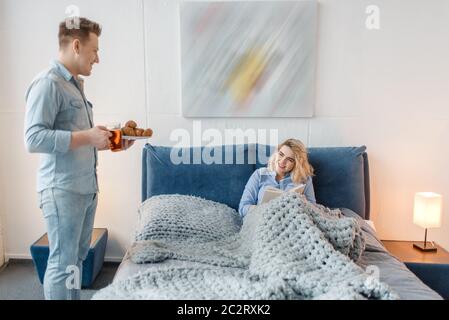 La coppia ama fare una colazione romantica a letto con croissant e biscotti. L'uomo e la donna mangiano dessert in camera da letto, Buongiorno. Stile di vita felice, il luogo Foto Stock