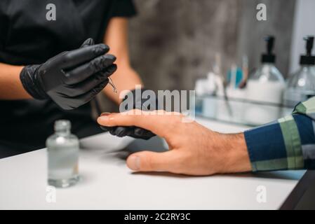 Estetista in nero Guanti chiodi di lucidatura per client maschio, vista dall'alto, uomini manicure in salone. Manicurist facendo per la cura delle mani procedura Foto Stock