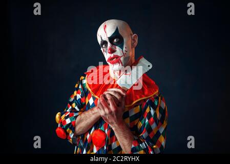 Mad sanguinosa clown con carne cleaver, circus orrore. L'uomo con il trucco in costume di carnevale, crazy maniac Foto Stock