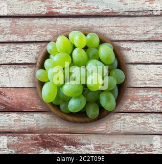 Uva in una ciotola di legno isolata su tavola di legno. Green Uves Kish Mish con spazio per la copia del testo. Uve mature e gustose su sfondo ligneo. Vet Foto Stock