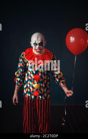 Brutto sanguinosa clown con il dito umano nella sua denti detiene il pallone aerostatico, horror. L'uomo con il trucco in costume di carnevale, crazy maniac Foto Stock