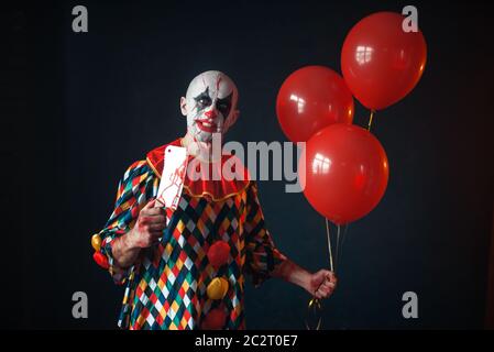 Brutto sanguinosa clown con carne cleaver detiene il pallone aerostatico, horror. L'uomo con il trucco in costume di carnevale, crazy maniac Foto Stock