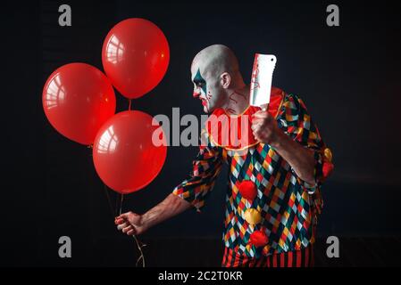 Scary sanguinosa clown con carne cleaver e pallone aerostatico di intrufolarsi in seminterrato, horror. Crazy maniac Foto Stock