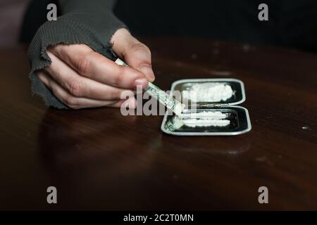 Dollaro rotolato in mani addict e dose di cocaina su specchio isolato su sfondo di legno. Foto Stock