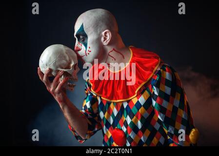 Mad sanguinosa clown detiene il teschio umano, horror. L'uomo con il trucco in costume di carnevale, crazy maniac Foto Stock