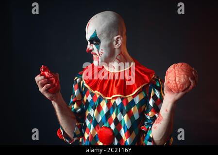 Mad sanguinosa clown detiene il cuore umano e il cervello. L'uomo con il trucco in costume di carnevale, crazy maniac Foto Stock