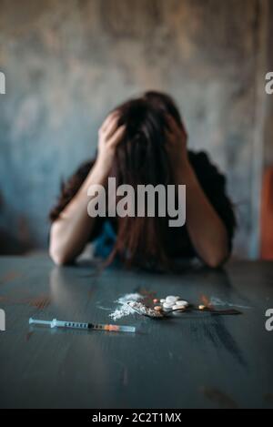 Femmina junkie seduto al tavolo con farmaci e siringa, grunge interno camera su sfondo. Concetto di tossicodipendenza, persone addicted Foto Stock