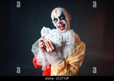 Scary sanguinosa clown con crazy occhi detiene il fan di denaro. L'uomo con il trucco in costume di carnevale, mad maniac Foto Stock