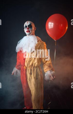 Mad sanguinosa clown con il trucco in costume di carnevale detiene il pallone aerostatico, crazy maniac, scary monster Foto Stock