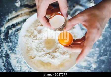 Un uomo ha rotto un uovo di pollo e sta andando mescolarlo con la farina in una ciotola per fare l'impasto. Cottura. Foto Stock