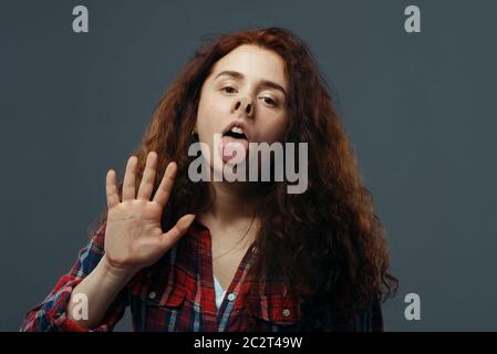 Viso e mano di giovane donna schiacciati su vetro trasparente. Donna in piedi alla vetrina con scomodo sguardo, umorismo, emozione espressione Foto Stock