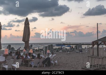 Tel Aviv/Israel-12/10/18: Persone che socializzano al tavolo in un'area salotto di un bar, situato sulla spiaggia di Tel Aviv al tramonto in un caldo evento estivo Foto Stock