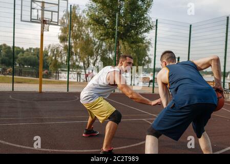 Due giocatori di basket che giocano un intenso match sul campo all'aperto. Gli atleti di sesso maschile in abbigliamento sportivo giocano il gioco su streetball allenamento Foto Stock