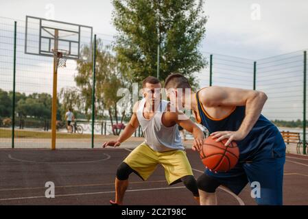 Due giocatori di basket che giocano un intenso match sul campo all'aperto. Gli atleti di sesso maschile in abbigliamento sportivo giocano il gioco su streetball allenamento Foto Stock