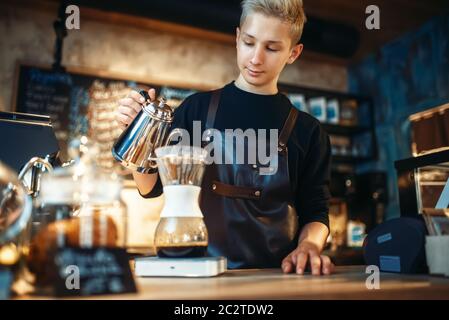 Giovane maschio barista rende il latte, il contatore di caffè e macchina espresso su sfondo. Barman lavora nella caffetteria, il barman prepara il caffè Foto Stock