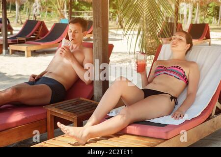 una giovane coppia riposa sui lettini e beve un cocktail. Foto Stock
