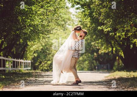 Felice sposo alza sposa nel parco estivo. Uomo alzato e abbraccio donna alle braccia. Coppia appena sposata nel parco. Solo matrimonio Foto Stock